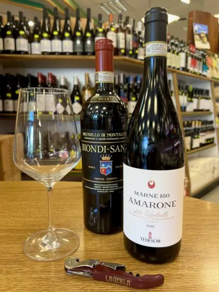 Bottiglia di Amarone in primo piano insieme a una selezione di vini rossi pregiati disponibili presso La Sorgente dell’Alimentazione D'Onofrio  a Roma.